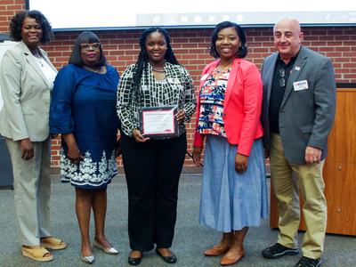 Five people standing in a row, center person holding a framed certificate