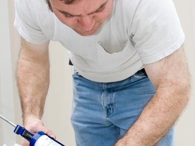 Handyman using a caulking gun to caulk a window.