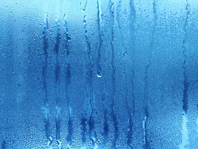 Condensation droplets and vertical water streaks on a blue-tinted glass surface