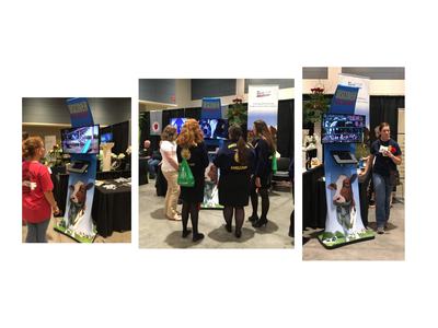 Trade show kiosk labeled DISCOVER NC DAIRY with cow graphic and attendees viewing screens