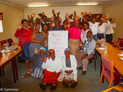 Group of people waving in a meeting room, holding sign "THANK YOU IAIA SA DELEGATE GROUP"