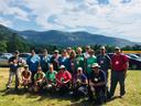 Group of people in hiking gear posing in a grassy lot with mountains behind