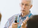 Older man with white hair and glasses holding a microphone while speaking at a meeting