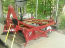 Red tractor-mounted tillage attachment secured with yellow straps on flat trailer