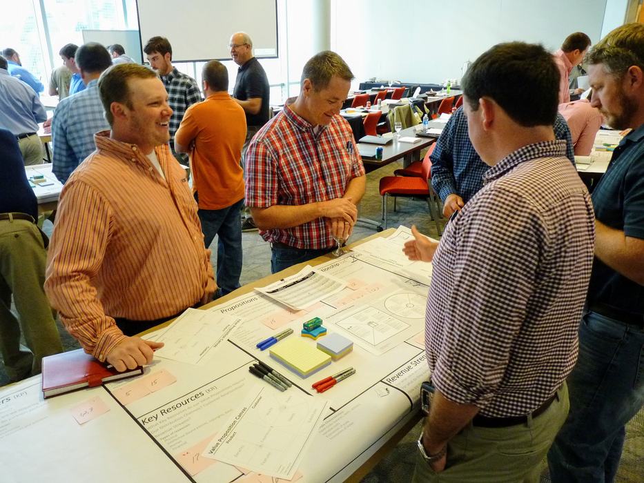 Several men standing around a table reviewing papers and a worksheet labeled "Key Resources"