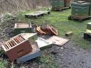 Overturned and stacked beehive boxes and frames beside intact beehives on muddy ground