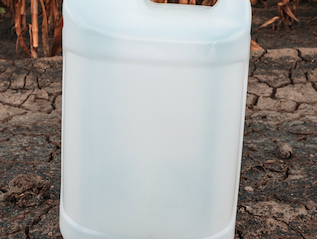 White plastic jerrycan with screw cap on cracked dry soil in front of dried corn stalks