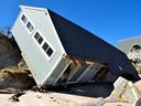 Coastal house toppled onto beach, partially detached from eroded bluff