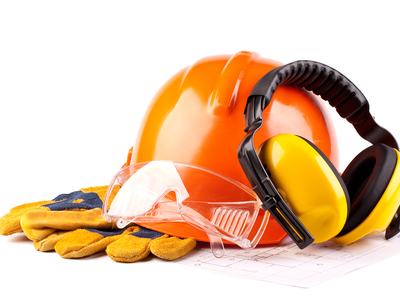 Orange hard hat with safety goggles, yellow earmuffs, and work gloves on blueprint