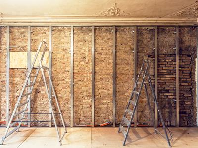 Exposed brick wall with metal studs and two A-frame ladders during renovation