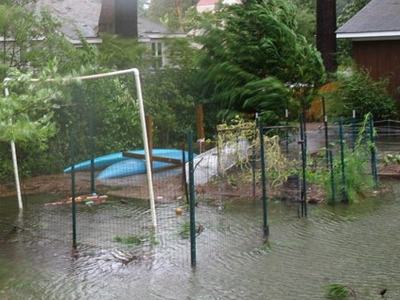 Backyard flooded, standing water covering lawn, fence, and an overturned inflatable pool