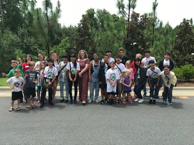 Group of children and adults standing on a road in front of trees