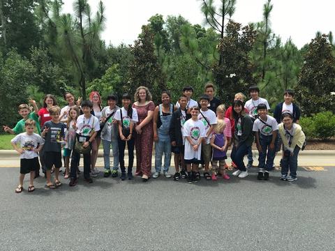 Group of children and adults standing on a road in front of trees