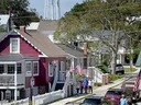 Small town street with parked cars, pedestrians on sidewalk, American flags, and water tower