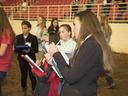 Girls standing in an indoor arena writing notes on clipboards