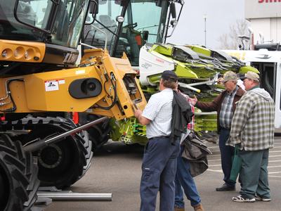 Group of men inspecting large agricultural machinery at outdoor exhibition