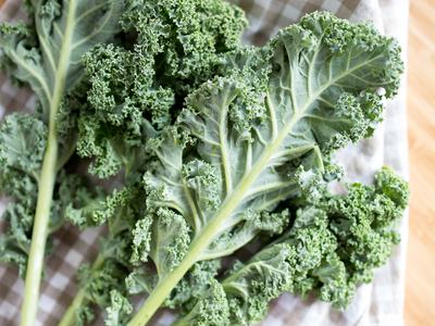 Fresh curly kale leaves on a checkered cloth over a wooden cutting board