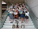 Group of young women on stairs holding plaques, ribbons and award plates with trophies below