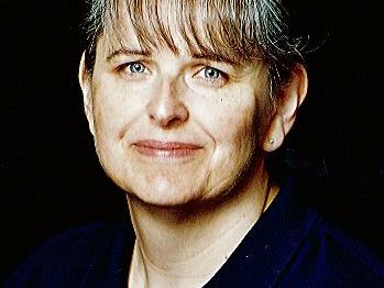 Middle-aged woman with bangs and blue eyes wearing a dark collared shirt on black background