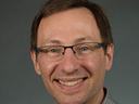 Adult man wearing glasses and a gray plaid shirt against a plain gray background