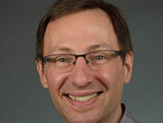 Adult man wearing glasses and a gray plaid shirt against a plain gray background