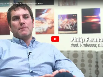 Man seated in interview setting; on-screen text: "Asst. Professor, Marketing"