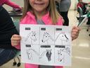 Young girl holding paper with six horse head sketches labeled STAR, SNIP, BLAZE, STRIP, BALD FACE, CHIN SPOT