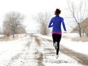 Runner in blue jacket jogging on a snowy rural dirt road, seen from behind