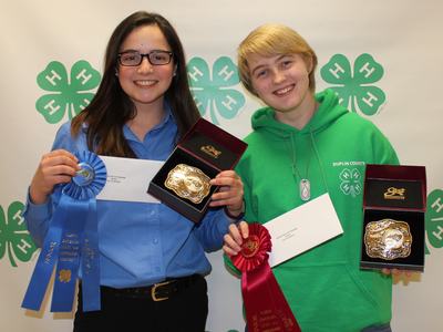 Two youth holding award belt boxes and ribbons in front of 4‑H clover backdrop; hoodie reads "Duplin County"