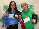 Two youth holding award belt boxes and ribbons in front of 4‑H clover backdrop; hoodie reads "Duplin County"