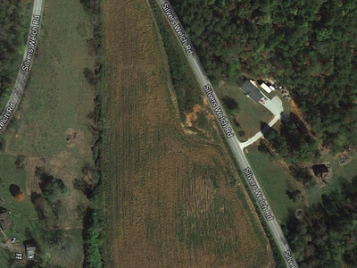 Triangular harvested field beside curved Silvers Welch Rd, adjoining forest and scattered buildings