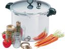 Large stainless pressure canner with glass jars, lids, a jar of pickles, tomatoes and carrots
