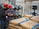 two men in red hard hats look at a tablet while standing in a feed mill