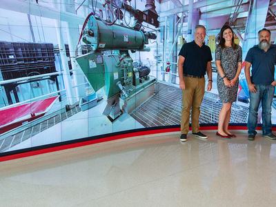 five people standing in front of a large screen showing a pellet mill