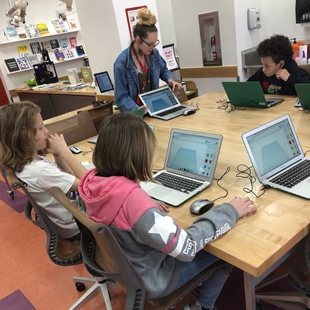 children with laptops seated around a table