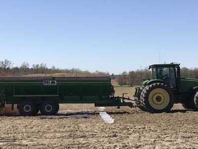 John Deere tracker pulling a litter spreader across a field