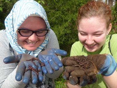 Two people holding muddy gloved hands presenting earthworms and soil