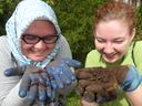 Two people holding muddy gloved hands presenting earthworms and soil