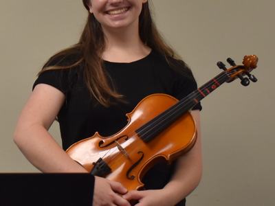 Person holding a violin across their torso, standing against a beige wall