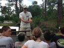 Man holding a small fish out toward a group of children watching outdoors