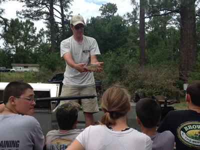 Man holding a small fish out toward a group of children watching outdoors