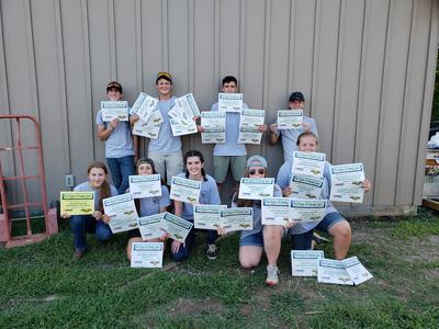 Group of youths holding "West Region 4‑H Shooting Sports" certificates against a building wall