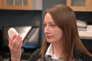 A woman standing in a lab looking at a fungal culture in a petri dish.