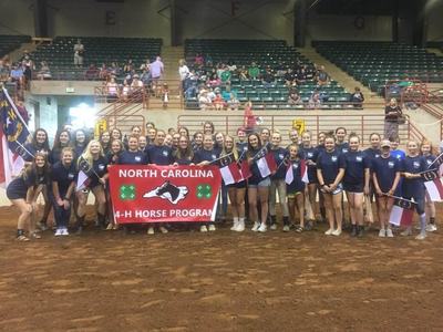 Group of youths holding banner "NORTH CAROLINA 4-H HORSE PROGRAM" in an indoor arena