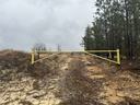 Yellow metal gate blocks sandy gravel road with trees on the right under cloudy sky