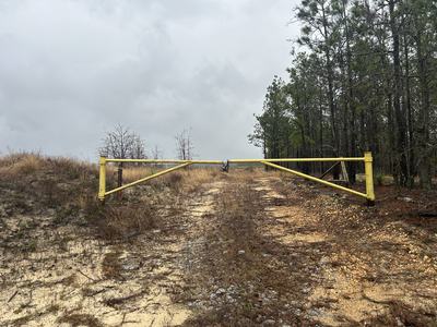 Yellow metal gate blocks sandy gravel road with trees on the right under cloudy sky