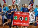 Group of youth carrying red banner reading "NORTH CAROLINA 4‑H HORSE PROGRAM" at indoor event