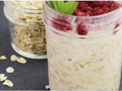 Jar of overnight oats topped with raspberries and a mint leaf, jar of dry oats behind