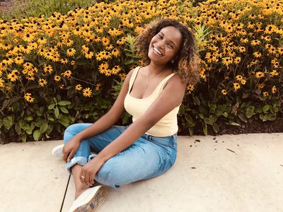 Young woman sitting cross-legged on sidewalk in front of a bed of yellow coneflowers