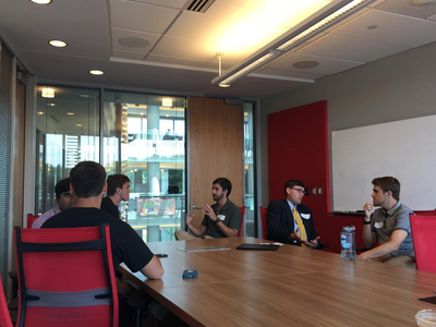 Six people seated around a conference table talking in a glass-walled meeting room